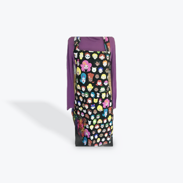 A reversible adult apron featuring a colorful pattern with character illustrations on one side and a multi color splatter on the reverse, with pockets on both sides.