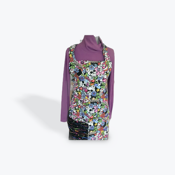 A reversible adult apron featuring a colorful pattern with skulls and queer  on one side and a black splatter pattern, with pockets on both sides.
