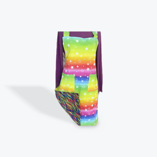 A reversible adult apron featuring a colorful pattern with a rainbow and starts on one side and a multi color pattern on the other, with pockets on both sides.